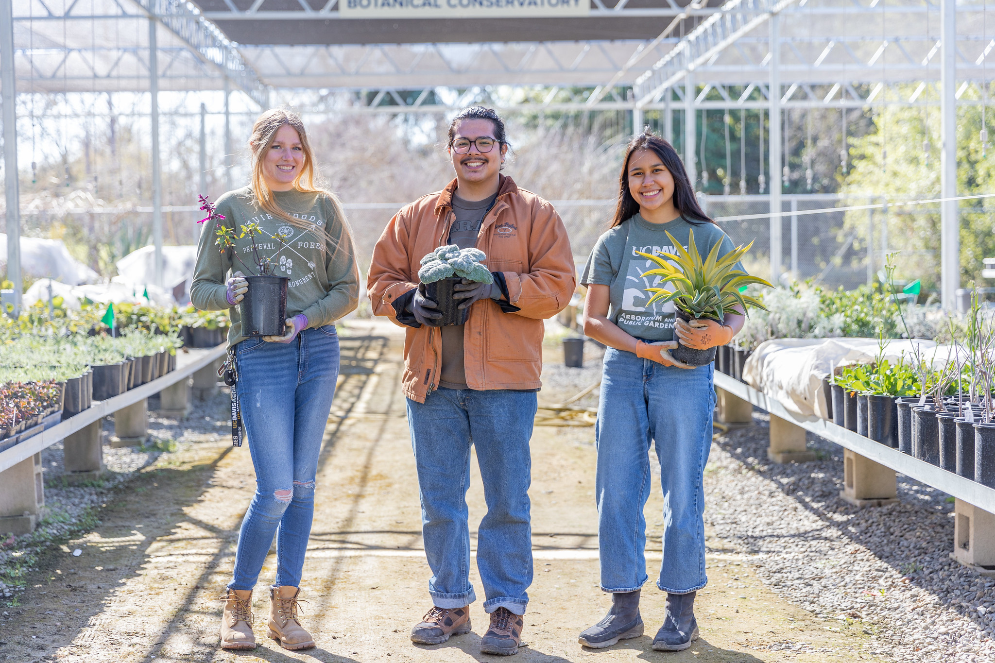 Three people holding plants, posing in the nursery