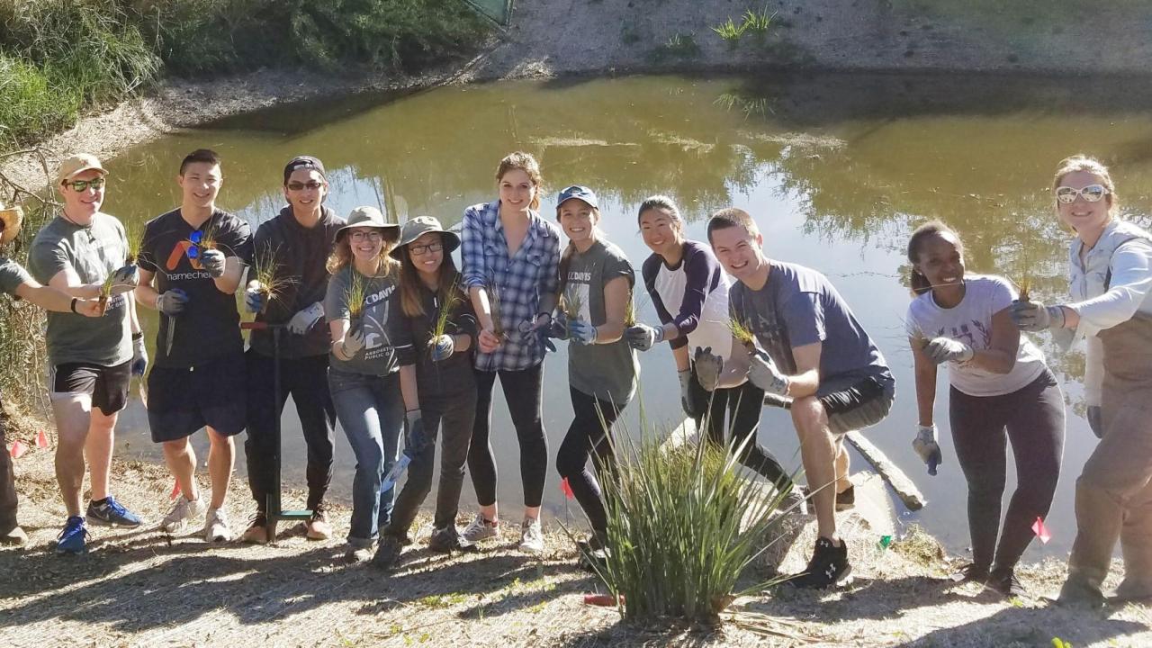 Students in the UC Davis Arboretum and Public Garden's Learning by Leading team smiling and posing by a pond, holding tools and equipment.