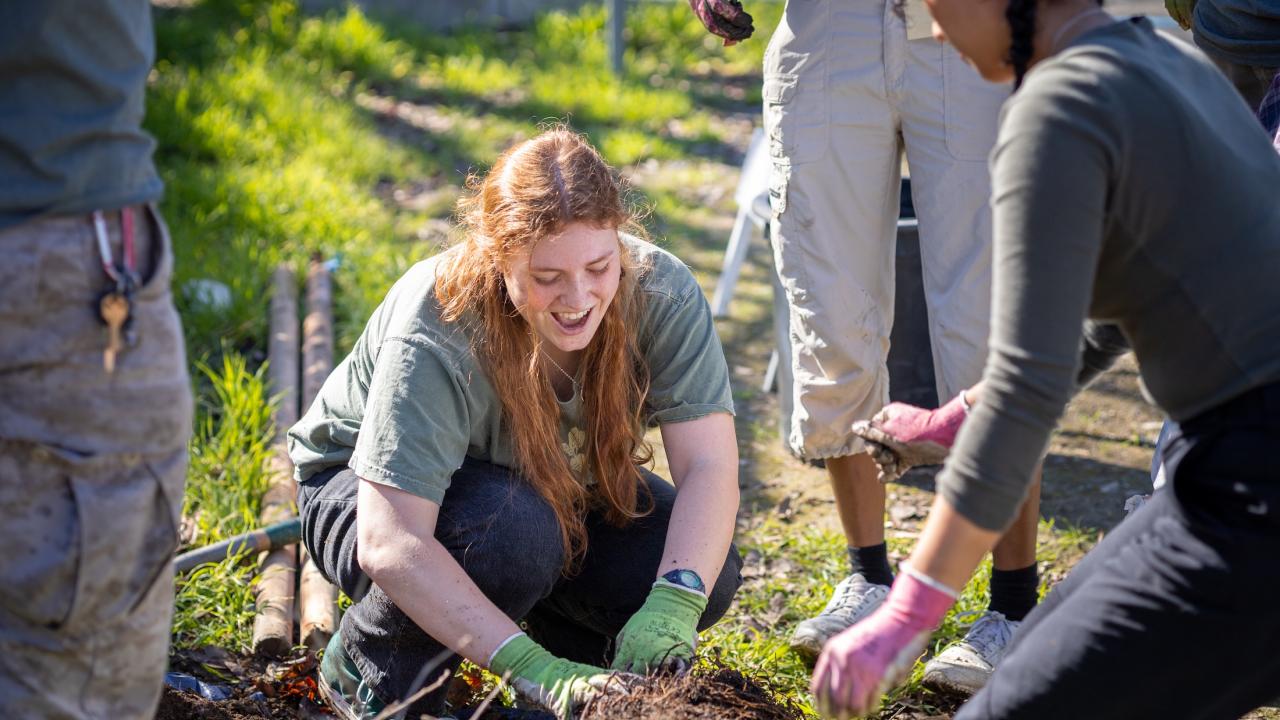 Person smiling while kneeling, among upturned soil among others