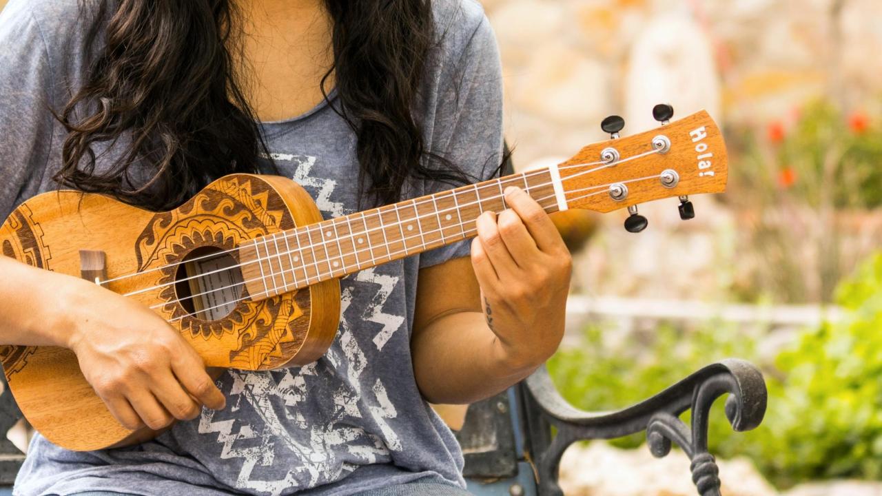 Person sits outdoors playing ukelele 