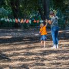 Image of student helping child place oak leaf on laundry line in UC Davis Shields Oak Grove.