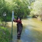 Two student interns pose smiling, wearing waders standing in Putah Creek